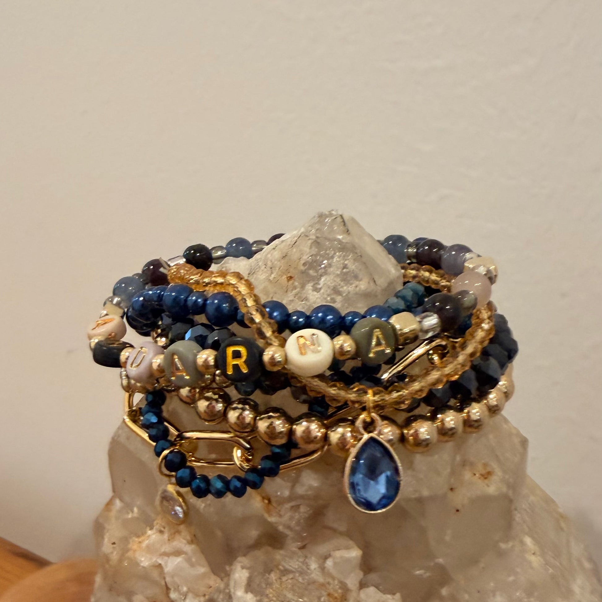 Stack of beaded bracelets with gold and blue accents on a rock