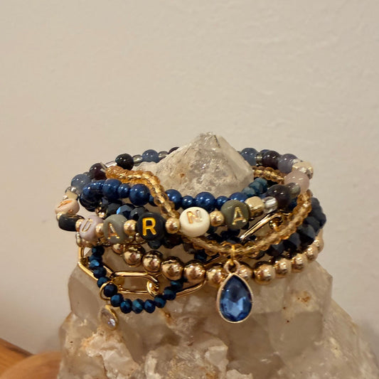 Stack of beaded bracelets with gold and blue accents on a rock